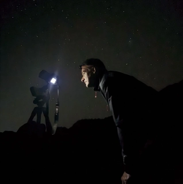 Michael Wells at night, lit by his camera's screen, beside a DSLR on a tripod under a star-filled sky in Teide National Park, Tenerife.